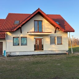 Expo-Activ - Nowy dom jednorodzinny z czerwoną dachówką i beżową elewacją w jesiennym krajobrazie. Okna zabezpieczone folią, widoczny garaż z brązową bramą.