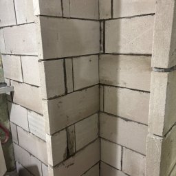 Expo-Activ - Wzniesiona ściana z białych bloczków betonu komórkowego, widoczny fragment narożnika. Szara zaprawa spoinuje bloki. Ujęcie z dołu, blisko ściany.