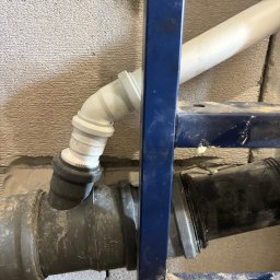 Expo-Activ - Instalacja kanalizacyjna podtynkowa w łazience w Kętrzynie. Rury z tworzywa sztucznego, szara ściana z betonu komórkowego, niebieski stelaż podtynkowy.