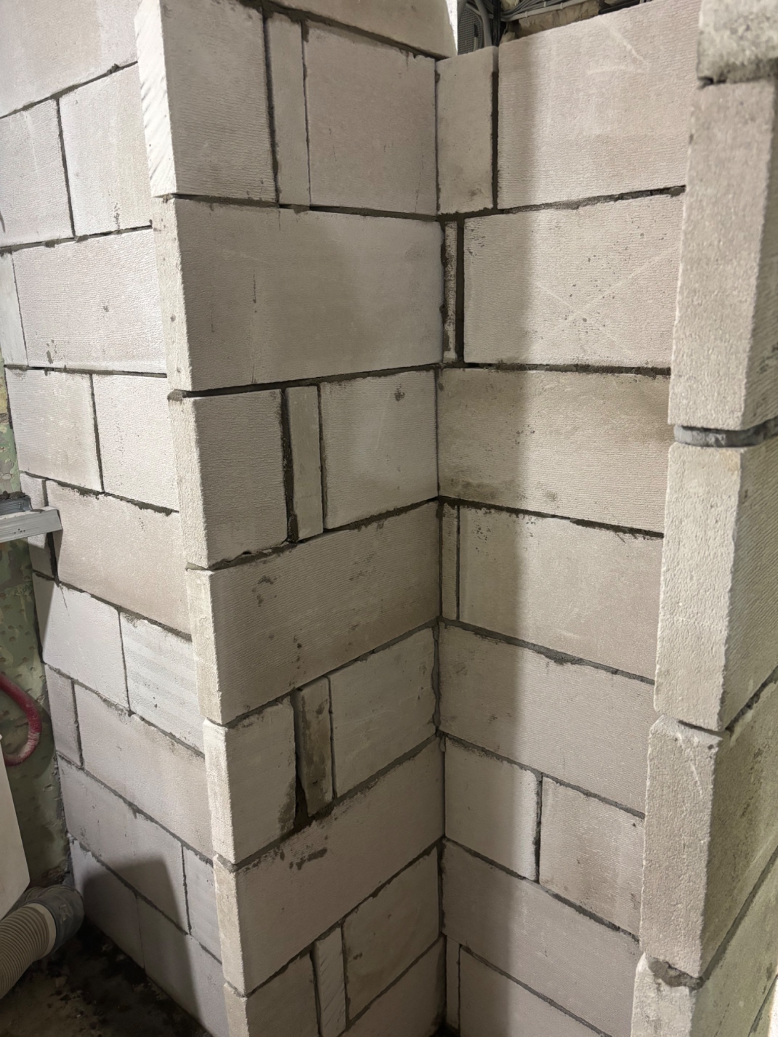 Wzniesiona ściana z białych bloczków betonu komórkowego, widoczny fragment narożnika. Szara zaprawa spoinuje bloki. Ujęcie z dołu, blisko ściany.