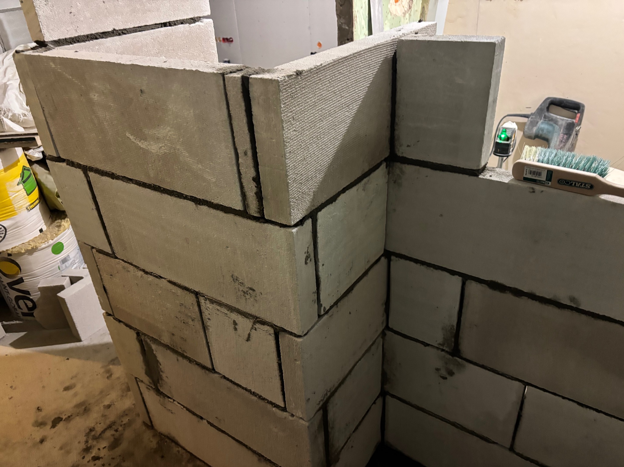 Wznoszenie ścianki działowej z betonu komórkowego w Kętrzynie. Widoczne narzędzia: poziomica i szczotka. Etap murowania, spoiny wypełnione zaprawą.