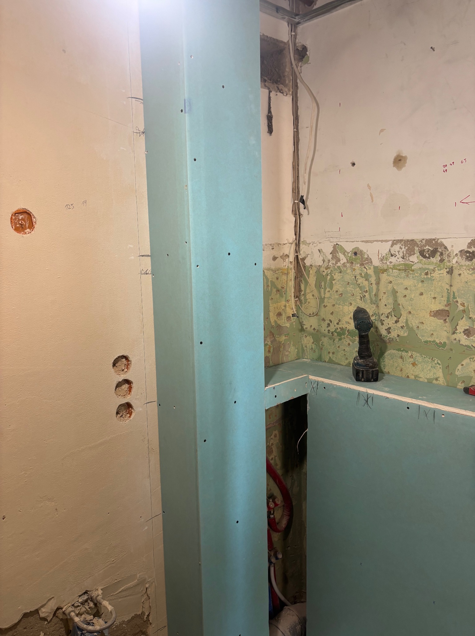 Wnętrze w trakcie prac: pionowa konstrukcja z płyty karton-gips, fragment ściany z instalacją elektryczną i fragment ściany z widocznymi śladami starej farby.