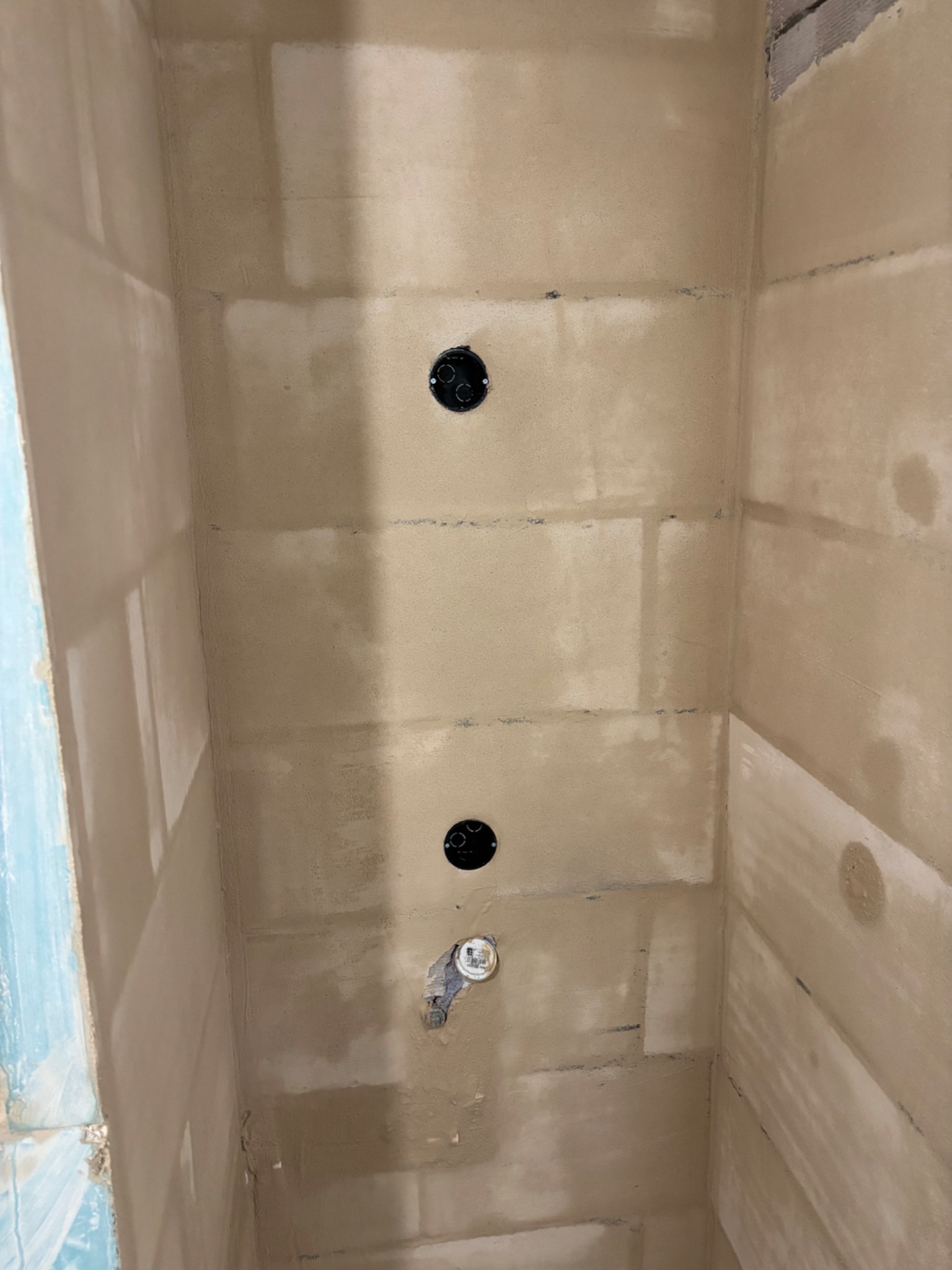 Ściany w trakcie tynkowania w łazience z widocznymi puszkami elektrycznymi i fragmentem niebieskiej ściany. Prace wykończeniowe w surowym wnętrzu.