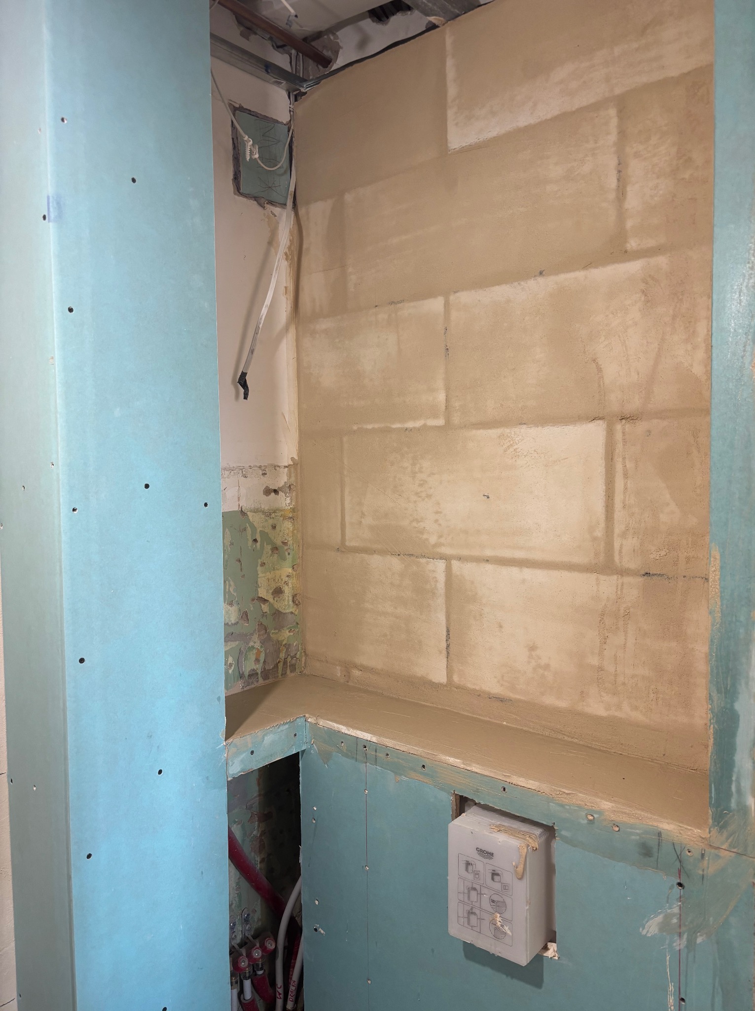 Ściana łazienki w trakcie prac: płyty gipsowo-kartonowe, fragmenty starej ściany, instalacja wodna i przygotowana ściana z bloczków do dalszego wykończenia.