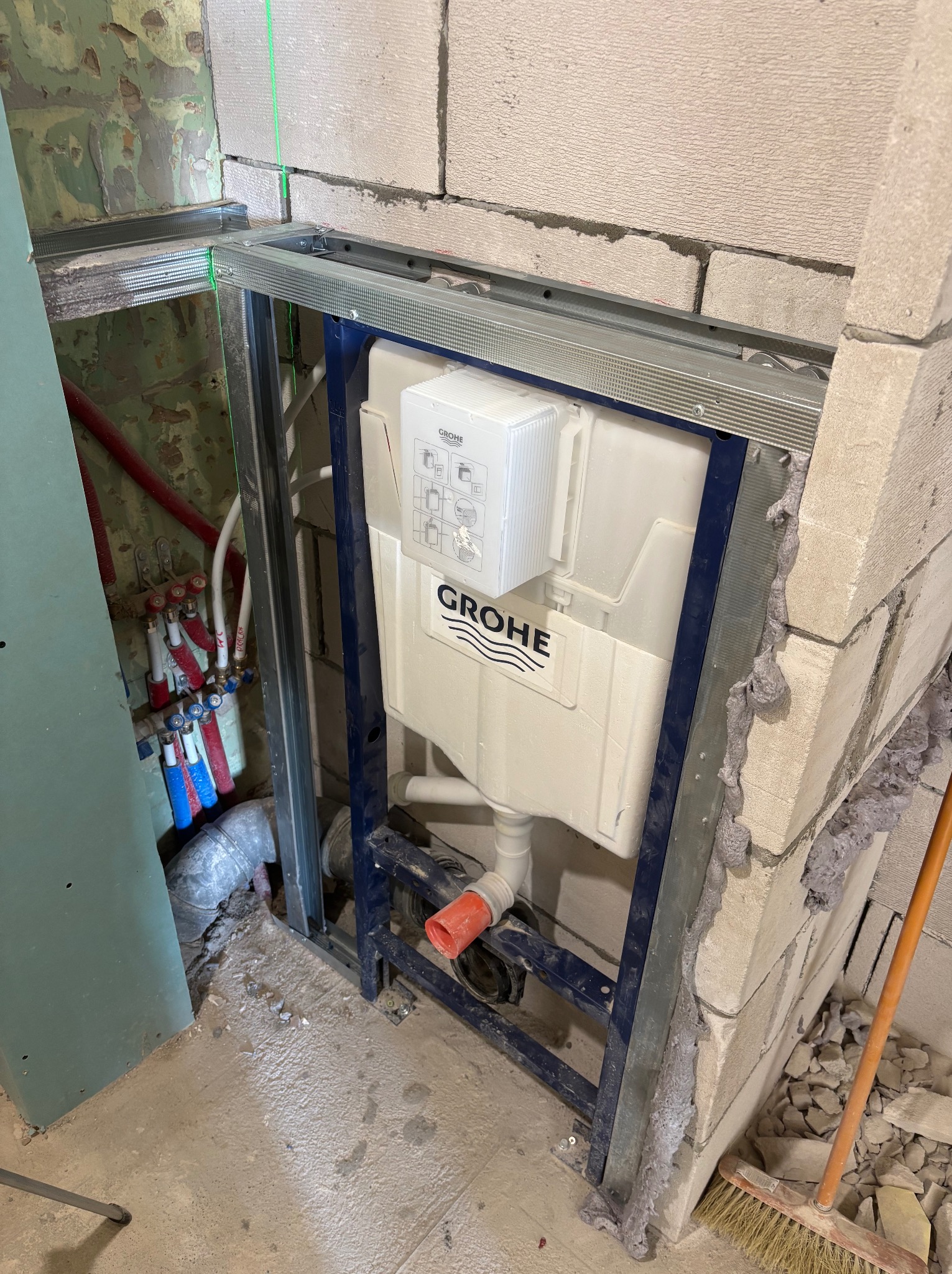 Stelaż podtynkowy Grohe zamontowany w łazience, widoczne instalacje wodne i kanalizacyjne, ściany z bloczków, metalowa konstrukcja, etap prac wykończeniowych.