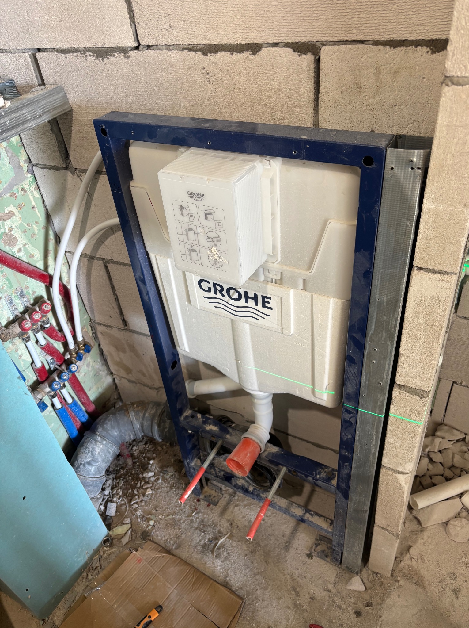 Stelaż podtynkowy Grohe zamontowany w surowej łazience, widoczne przyłącza wodne i kanalizacyjne. Laserowy poziom wskazuje na precyzję montażu.