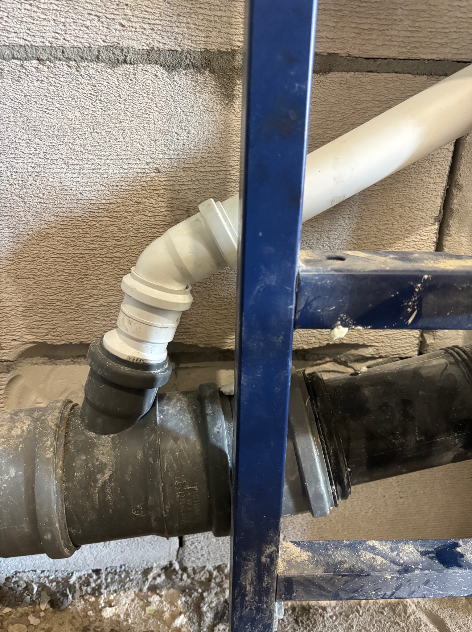 Instalacja kanalizacyjna podtynkowa w łazience w Kętrzynie. Rury z tworzywa sztucznego, szara ściana z betonu komórkowego, niebieski stelaż podtynkowy.