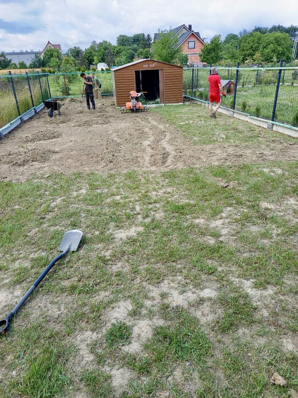 Działka po przekopaniu glebogryzarką, przygotowana pod nasadzenia. W tle pracownicy i narzędzia ogrodnicze.