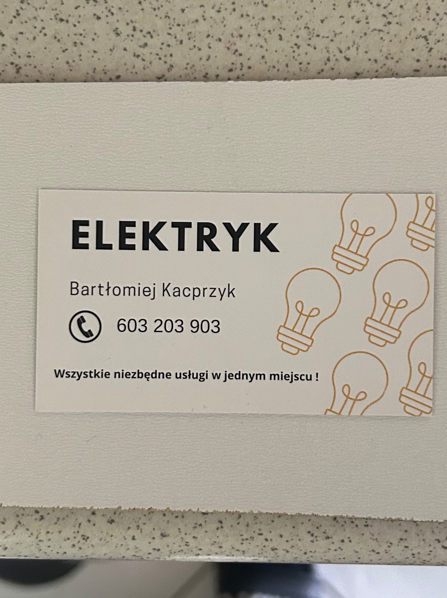 Wizytówka elektryka Bartłomieja Kacprzyka z numerem telefonu 603 203 903 i hasłem: Wszystkie niezbędne usługi w jednym miejscu! Tło wizytówki zdobią grafiki żarówek.