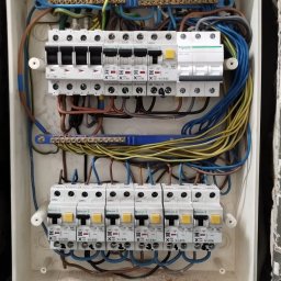 SPEC ZŁOTA RĄCZKA 24h Łodz okolice.Elektryka,Hydraulika. - Otwarta skrzynka elektryczna z bezpiecznikami, widoczne przewody w kolorach: niebieskim, żółtym i brązowym. Instalacja w trakcie podłączania, detale montażu.
