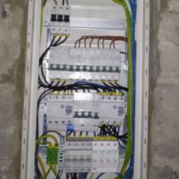 SPEC ZŁOTA RĄCZKA 24h Łodz okolice.Elektryka,Hydraulika. - Kompletna, nowa rozdzielnia elektryczna w białej obudowie, z widocznymi zabezpieczeniami i okablowaniem, zamontowana na surowej, betonowej ścianie.