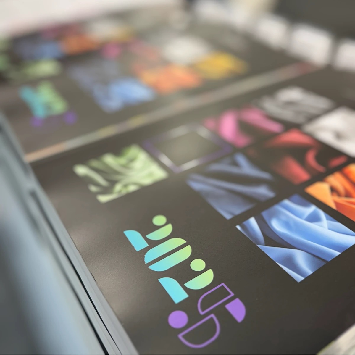Stos arkuszy z wydrukowanymi próbkami kolorów i logotypem '2025' w gradientowych barwach. Wydruk na czarnym tle, widoczne detale tekstur.