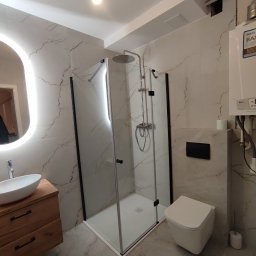 Projekt Home - Nowoczesna łazienka z kabiną prysznicową typu walk-in, umywalką na drewnianej szafce i podświetlanym lustrem. Ściany wykończone marmurkową płytką.