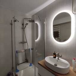 Projekt Home - Nowoczesna łazienka po remoncie z kabiną prysznicową typu walk-in, umywalką nablatową i podświetlanym lustrem. Minimalistyczny design z geometrycznym wzorem na ścianie.
