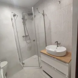 Nowoczesna łazienka: kabina prysznicowa narożna, umywalka nablatowa na szafce z drewnianym blatem, dekoracyjne płytki w geometryczne wzory.