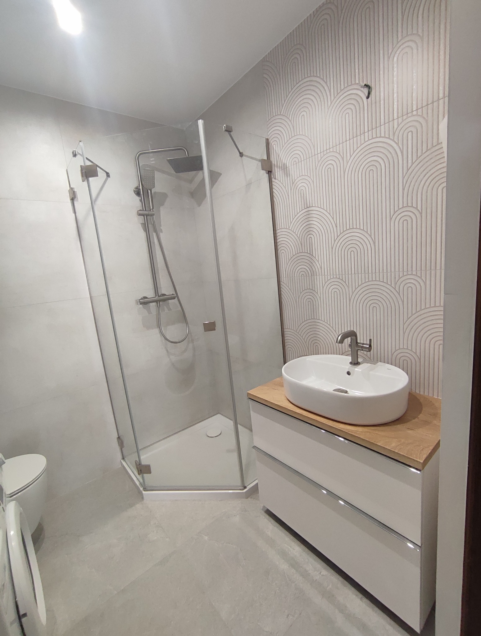 Nowoczesna łazienka: kabina prysznicowa narożna, umywalka nablatowa na szafce z drewnianym blatem, dekoracyjne płytki w geometryczne wzory.