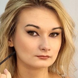 Renata Czapska - Portret kobiety z blond włosami i wyraźnym makijażem oczu typu kocie oko, podkreślone usta i delikatny róż na policzkach. W kadrze dłoń z pędzlem.
