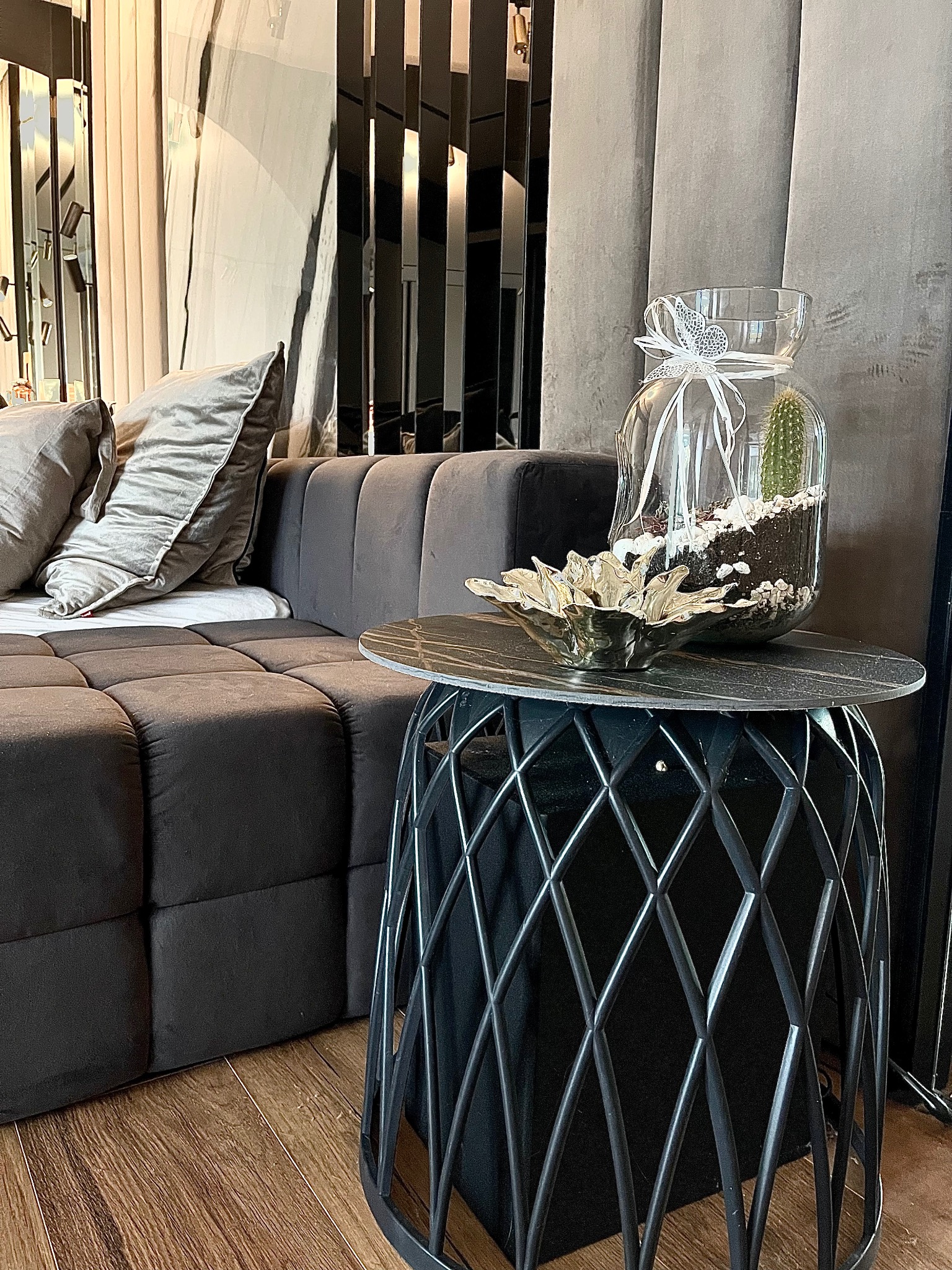Stylowy salon z ciemnoszarą sofą modułową, stolikiem z metalową podstawą i szklanym wazonem z kaktusem, element aranżacji wnętrza.