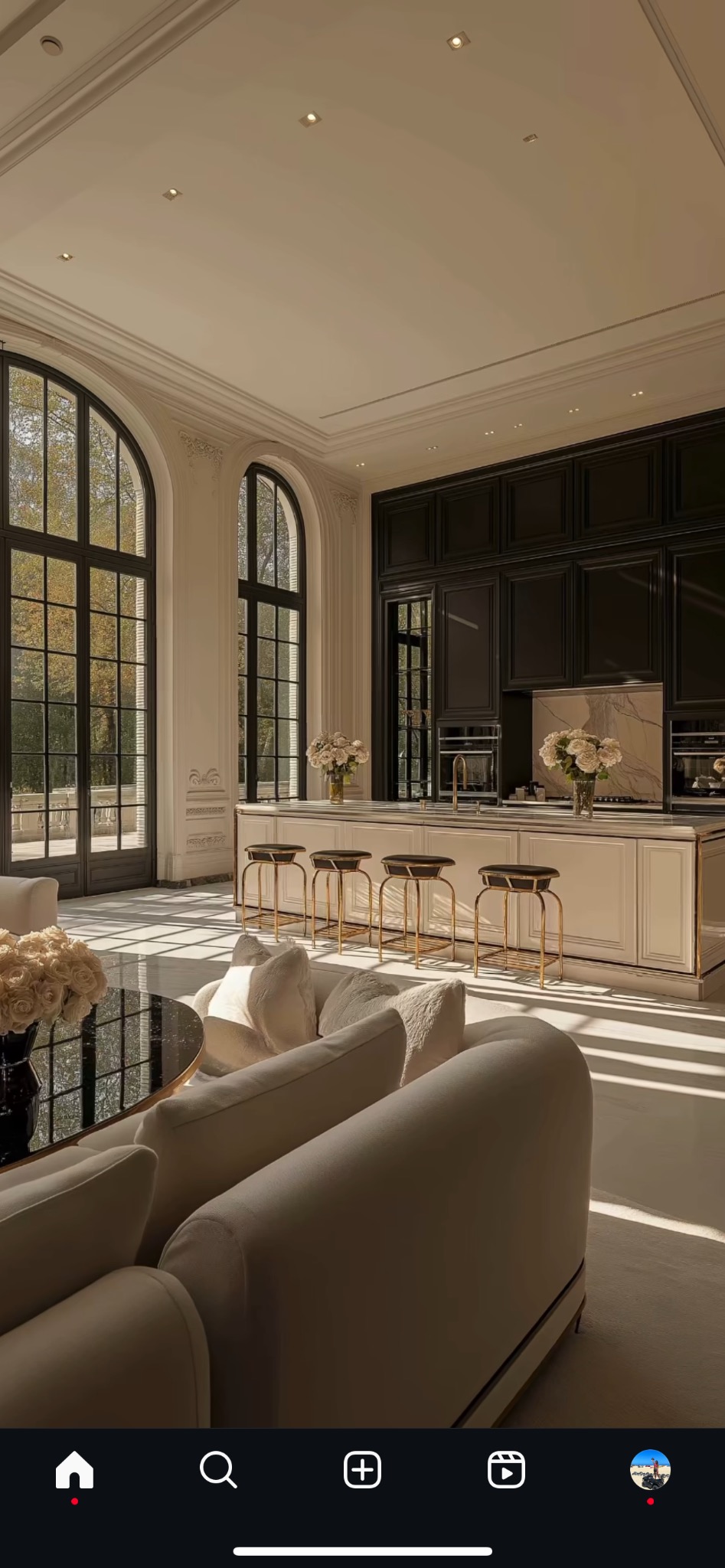 Eleganckie wnętrze: salon z kuchnią w stylu glamour. Wysokie okna łukowe, marmurowe podłogi, kremowe sofy i czarne szafki kuchenne z białym blatem.