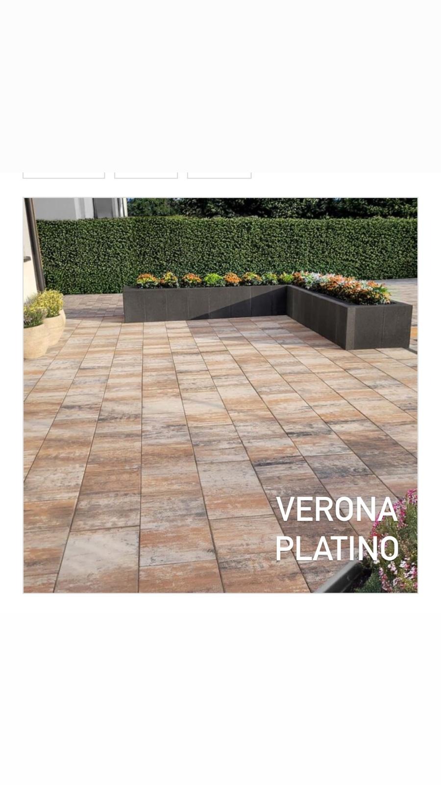 Ułożona kostka brukowa Verona Platino tworząca patio z zielonym żywopłotem w tle i donicami z kwiatami. Widok na zewnątrz, w dziennym świetle.