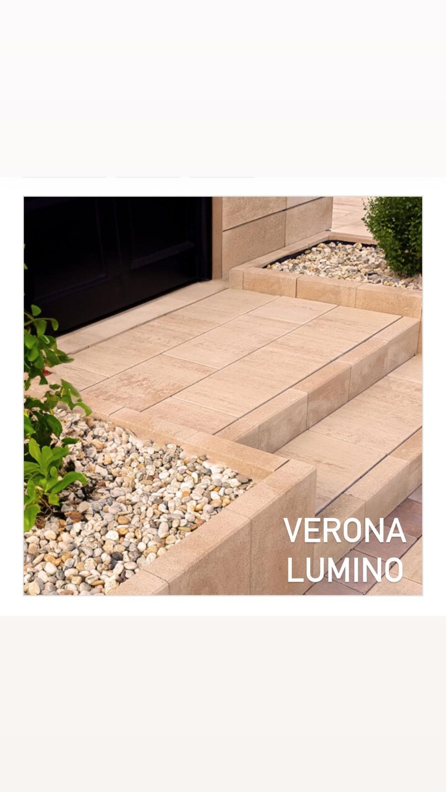 Wykończone schody wejściowe z beżowych płyt, z dekoracyjnym żwirkiem i roślinnością. Widoczne drzwi wejściowe i fragment elewacji.