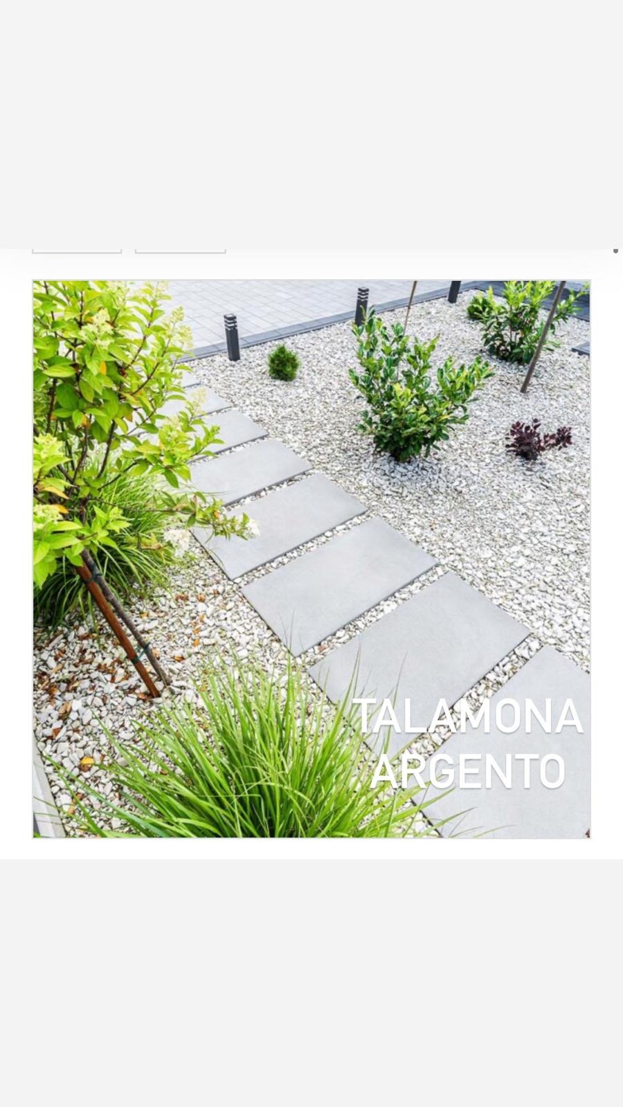 Ścieżka z płyt betonowych w ogrodzie wysypanym białym żwirem, z ozdobnymi krzewami i trawami. Widoczne lampy ogrodowe. Minimalistyczny design.