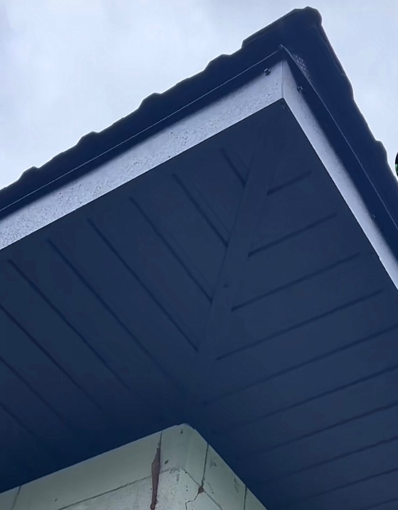 Ciemna podbitka dachowa z widocznymi poziomymi panelami i narożnikiem budynku z widocznymi pęknięciami, sfotografowana z dołu pod kątem.