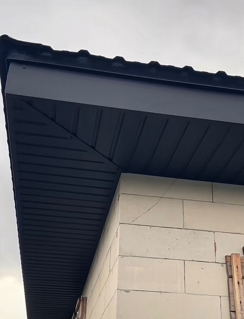 Nowoczesne, czarne podbitki dachowe z widocznym fragmentem dachu i ścianą budynku z białego bloczka. Ujęcie z dołu podkreśla geometrię konstrukcji.