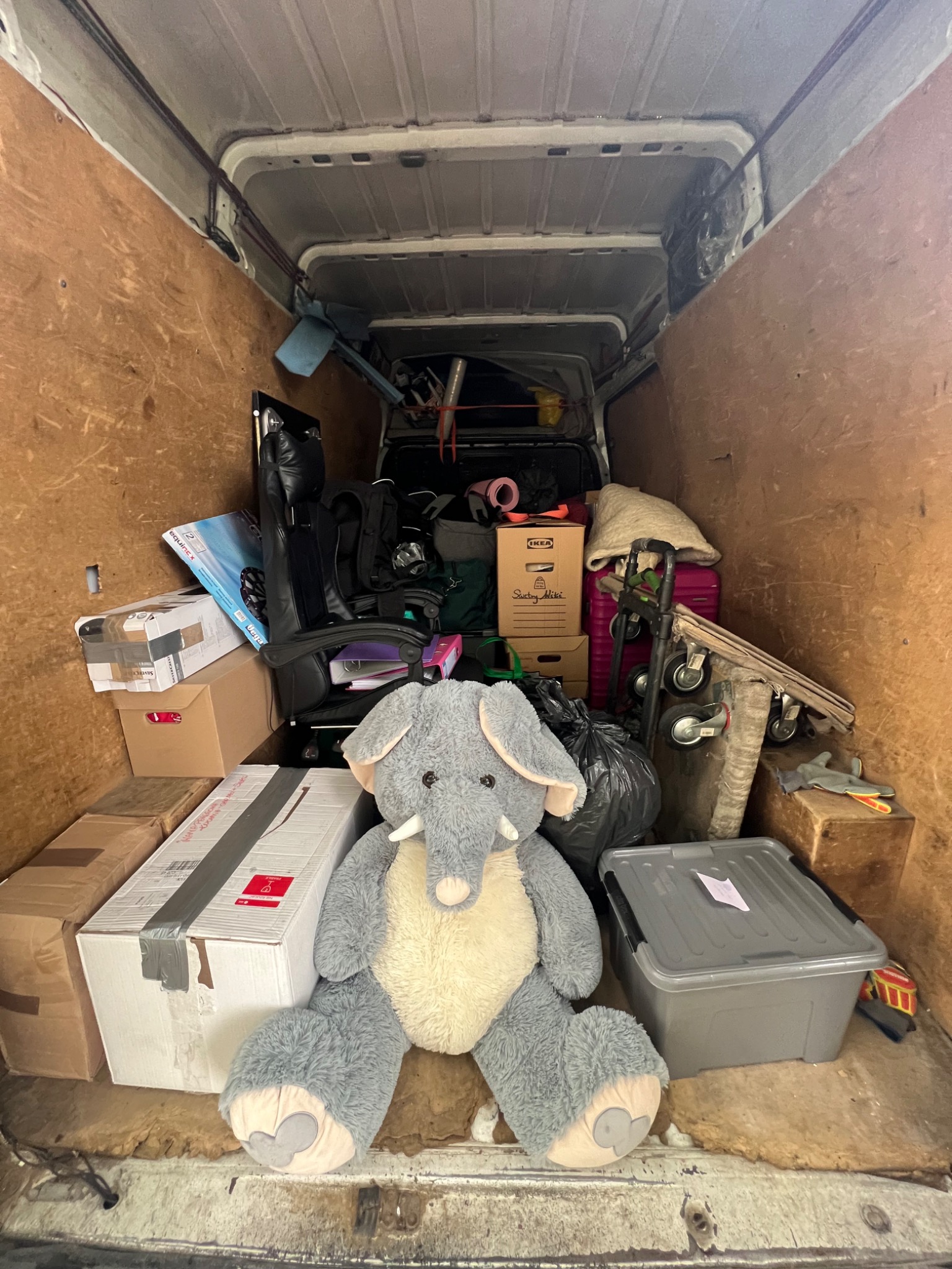 Wnętrze furgonetki załadowane kartonami, meblami i pluszowym słoniem. Widok z tyłu pojazdu, ukazujący przygotowania do transportu.