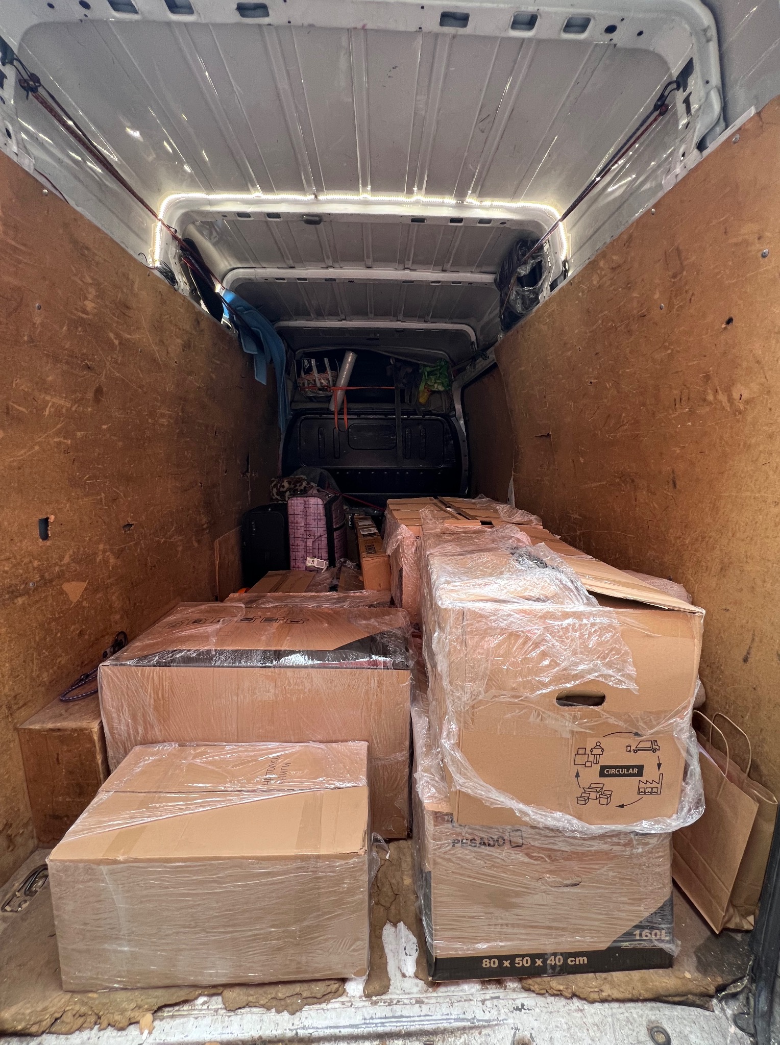 Kartonowe pudła zabezpieczone folią w przestrzeni ładunkowej busa z drewnianą zabudową, gotowe do transportu. Widok z wnętrza pojazdu.