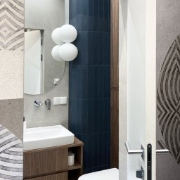 MOCHO STUDIO MONIKA MACHOWSKA-ALEKSANDROWICZ - Nowoczesna łazienka z umywalką nablatową, okrągłym lustrem i oryginalnym oświetleniem w postaci białych kul. Ciemne płytki i drewniane szafki dodają elegancji.