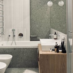 MOCHO STUDIO MONIKA MACHOWSKA-ALEKSANDROWICZ - Nowoczesna łazienka z wanną, bidetem i umywalką na drewnianej szafce. Ściany wykończone płytkami w odcieniach szarości. Widoczne akcesoria łazienkowe i oświetlenie.