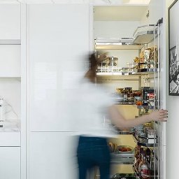 MOCHO STUDIO MONIKA MACHOWSKA-ALEKSANDROWICZ - Biała kuchnia z nowoczesnym systemem cargo: wysuwane półki pełne produktów spożywczych. Marmurowy blat, minimalistyczny design.