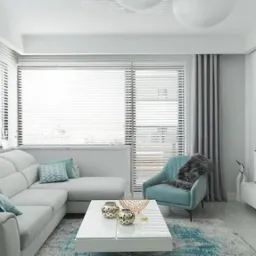 Nowoczesny salon w bieli i szarości z akcentami turkusu: sofa narożna, fotel, stolik kawowy, żaluzje okienne i dekoracyjny kominek elektryczny. Subtelne oświetlenie.