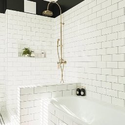 MOCHO STUDIO MONIKA MACHOWSKA-ALEKSANDROWICZ - Biała łazienka z wanną obudowaną płytkami, armaturą w kolorze starego złota i dywanem w orientalny wzór. Czarny pas na górze ściany dodaje kontrastu.