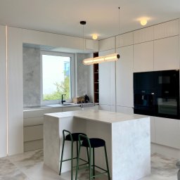 MOCHO STUDIO MONIKA MACHOWSKA-ALEKSANDROWICZ - Nowoczesna kuchnia w jasnych barwach z wyspą i zielonymi hokerami, oświetlona podłużną lampą. Minimalistyczny design, zabudowa kuchenna z teksturą.