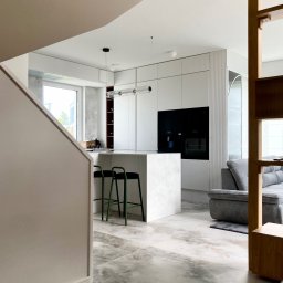 MOCHO STUDIO MONIKA MACHOWSKA-ALEKSANDROWICZ - Nowoczesna, otwarta kuchnia z wyspą i zielonymi hokerami. Marmurowe płytki podłogowe, białe szafki z frezowanymi frontami i czarny sprzęt AGD w zabudowie.