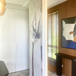 Nowoczesny przedpokój z szafą w zabudowie, tapetą z motywem roślinnym i designerską konsolą. Całość utrzymana w jasnej, stonowanej kolorystyce z akcentami drewna.