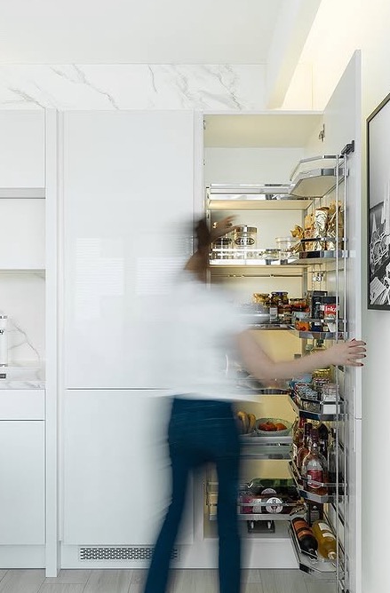 Biała kuchnia z nowoczesnym systemem cargo: wysuwane półki pełne produktów spożywczych. Marmurowy blat, minimalistyczny design.