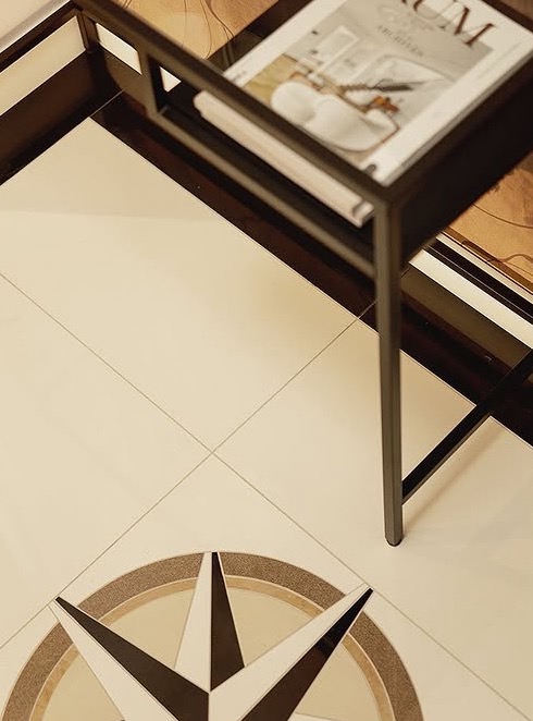 Jasne płytki podłogowe z dekoracyjnym motywem kompasu w Gdyni. Na płytkach stolik z magazynem wnętrzarskim. Detal wykończenia podłogi.