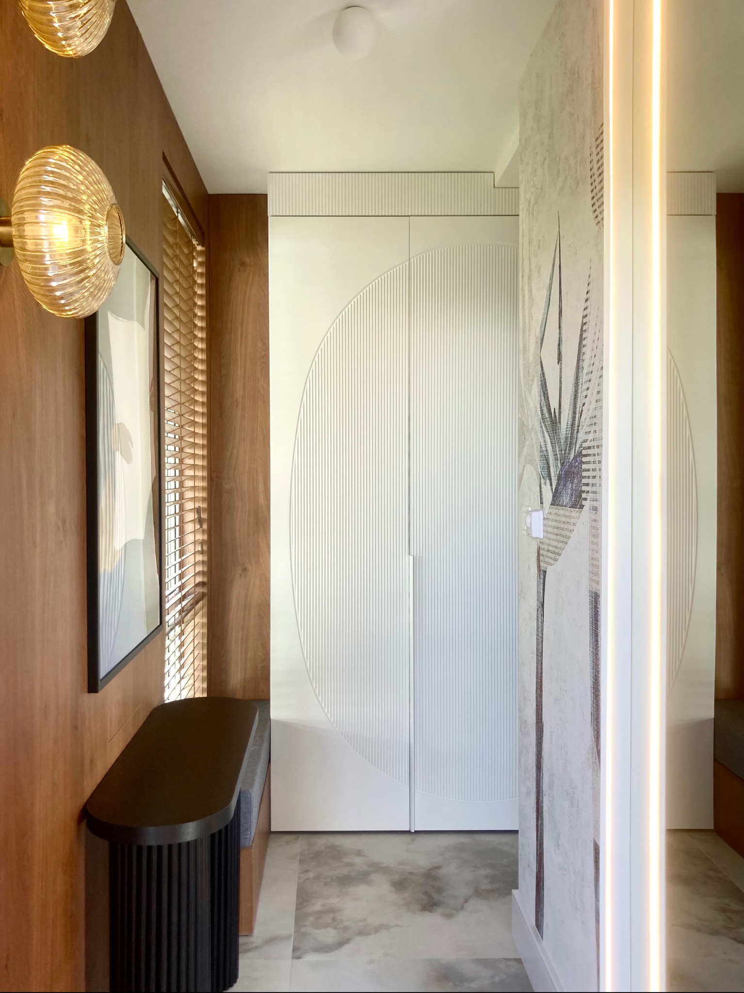 Nowoczesny przedpokój: białe szafy z frezowanymi okręgami, drewniane panele, marmurowa podłoga i designerskie oświetlenie.