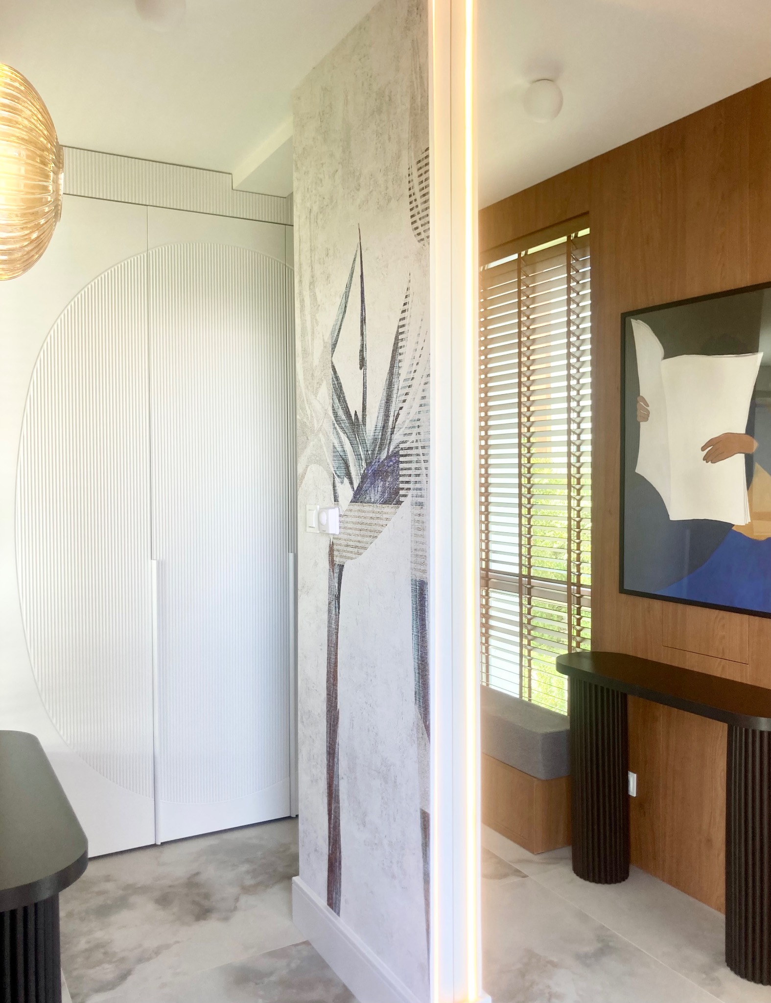 Nowoczesny przedpokój z szafą w zabudowie, tapetą z motywem roślinnym i designerską konsolą. Całość utrzymana w jasnej, stonowanej kolorystyce z akcentami drewna.