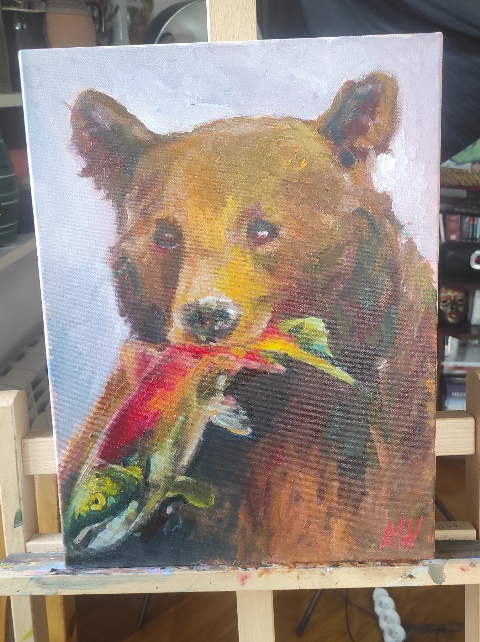 Obraz olejny na płótnie przedstawia brązowego niedźwiedzia trzymającego w pysku kolorową rybę. Widoczny fragment sztalugi i sygnatura autora w prawym dolnym rogu.