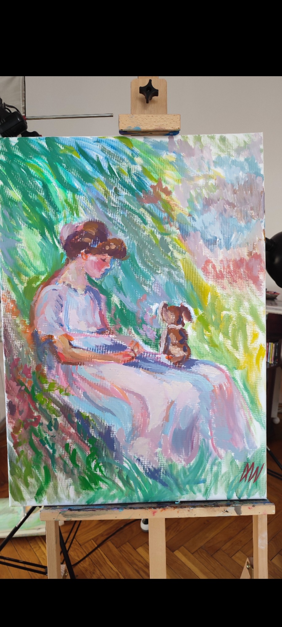 Obraz olejny na płótnie przedstawia kobietę z psem w ogrodzie, w stylu impresjonistycznym. Widoczne pociągnięcia pędzla i pastelowa kolorystyka. Obraz stoi na drewnianej sztaludze.