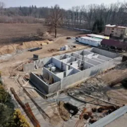 Zalane fundamenty domu z betonu komórkowego, widok z góry. Elementy konstrukcyjne tworzą układ pomieszczeń przyszłego budynku. W tle widoczne drzewa i budynek.