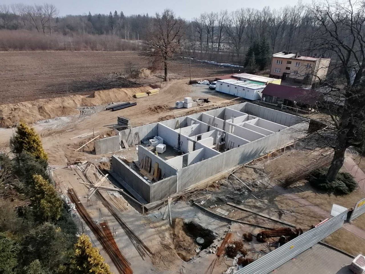 Zalane fundamenty domu z betonu komórkowego, widok z góry. Elementy konstrukcyjne tworzą układ pomieszczeń przyszłego budynku. W tle widoczne drzewa i budynek.