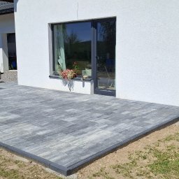 Bager Kop - Szara kostka brukowa ułożona na tarasie przylegającym do białego budynku z oknem, na którym stoją kwiaty. Z boku zaparkowany srebrny samochód.