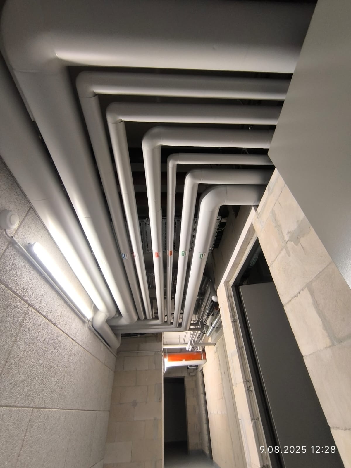 Białe rury instalacyjne pod sufitem w surowym wnętrzu, widok z dołu, układ równoległy z oznaczeniami kolorystycznymi.