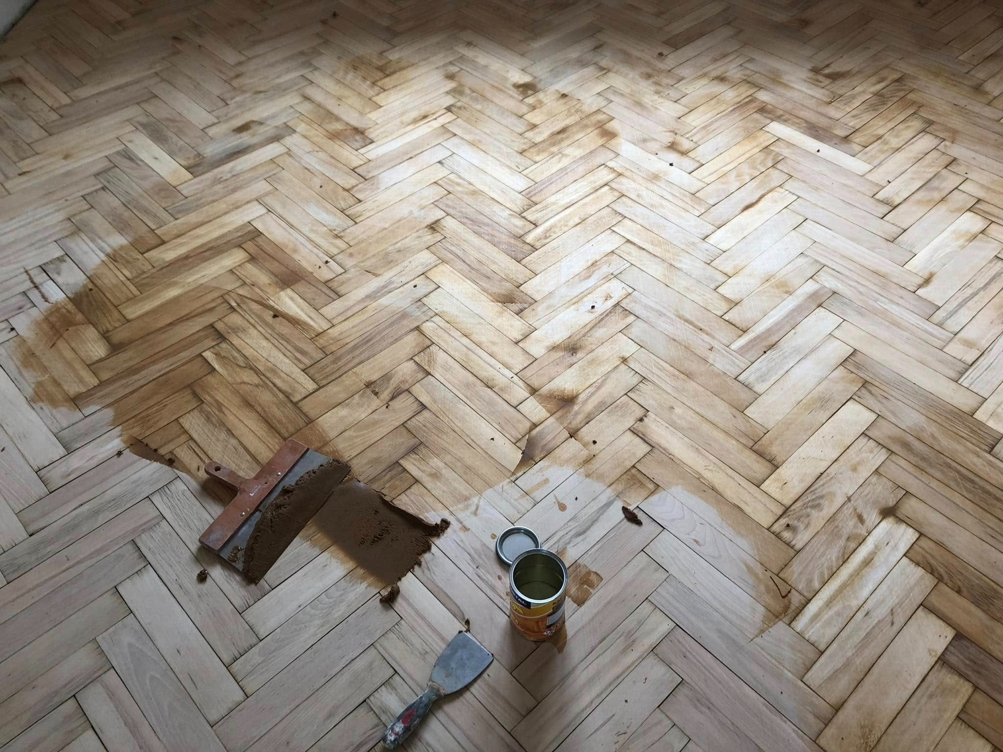 Parkiet w jodełkę podczas olejowania. Widoczne narzędzia, puszka z olejem i ślady po aplikacji. Część podłogi już zaolejowana, reszta surowa.