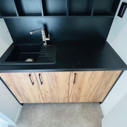 MIĘDZY SĘKAMI JAKUB WIERNICKI-BALCER - Nowoczesna zabudowa kuchenna z czarnym blatem i drewnopodobnymi frontami szafek, widok z góry, minimalistyczny design. Bateria Ferolli.